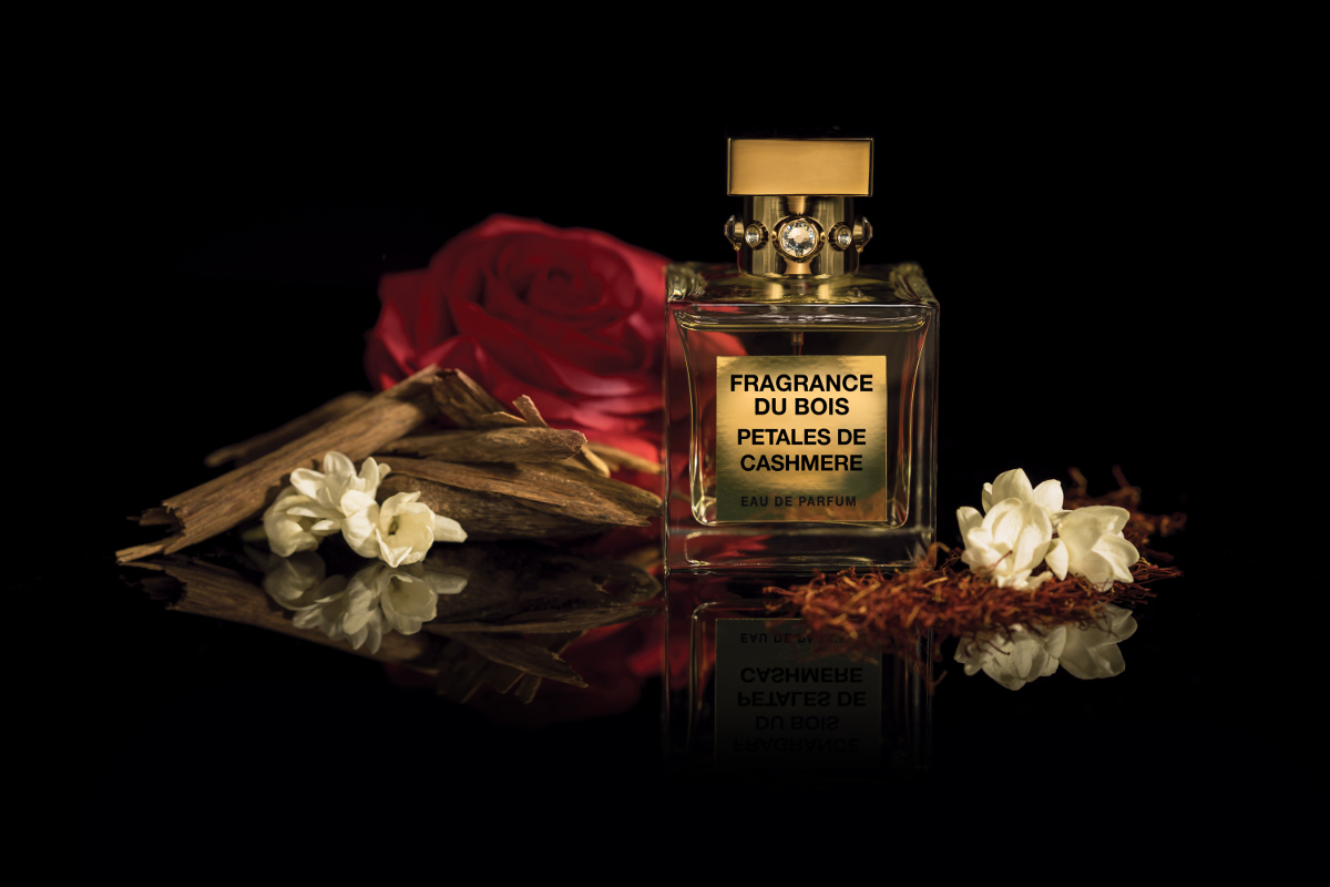 a bottle Petales de Cashmere next to a red rose, a pile of wood chips and small white blossoms