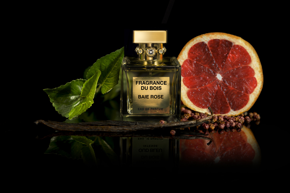 A bottle of Baie Rose perfume next to a grapefruit and vanilla pods