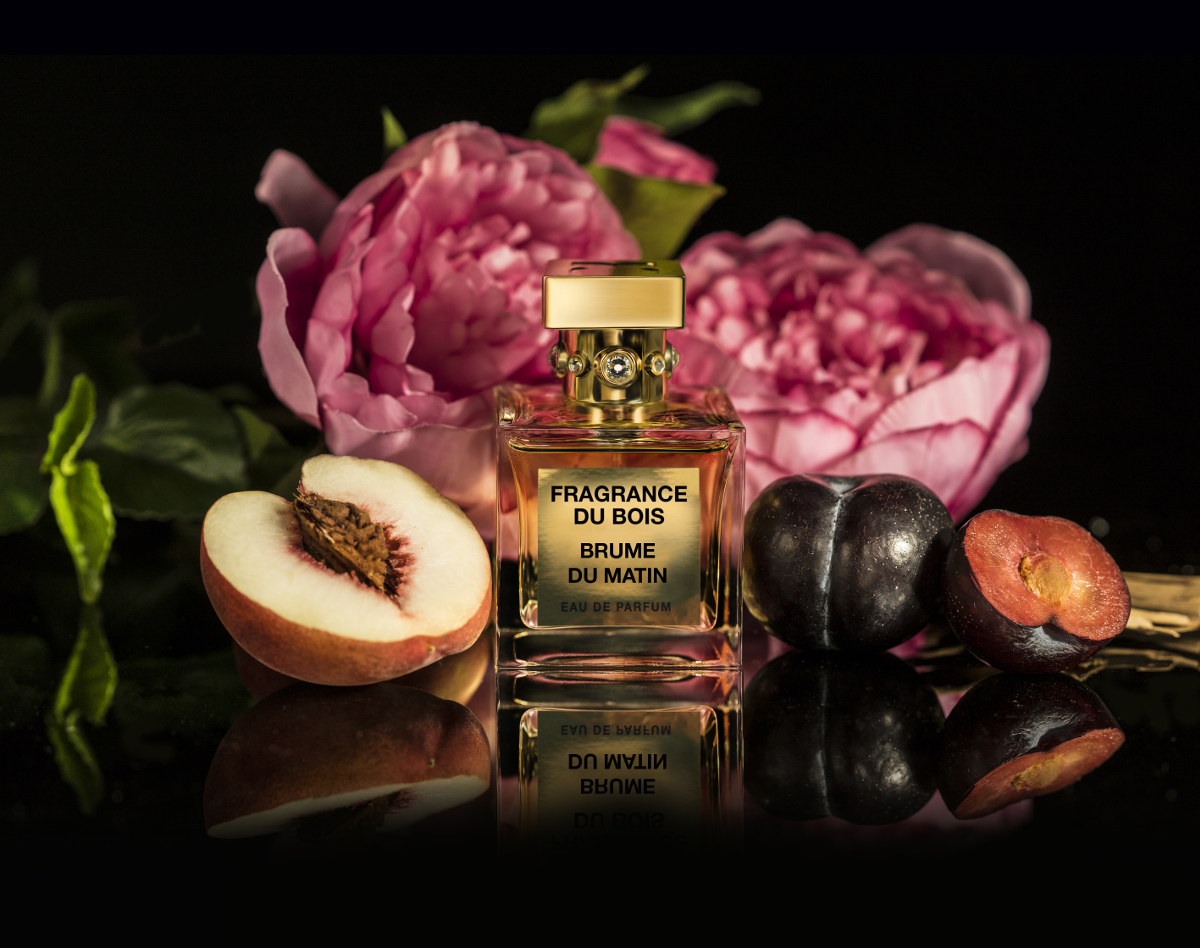 a bottle of Brume du Matin in front of a pink rose, with a peach and a plum