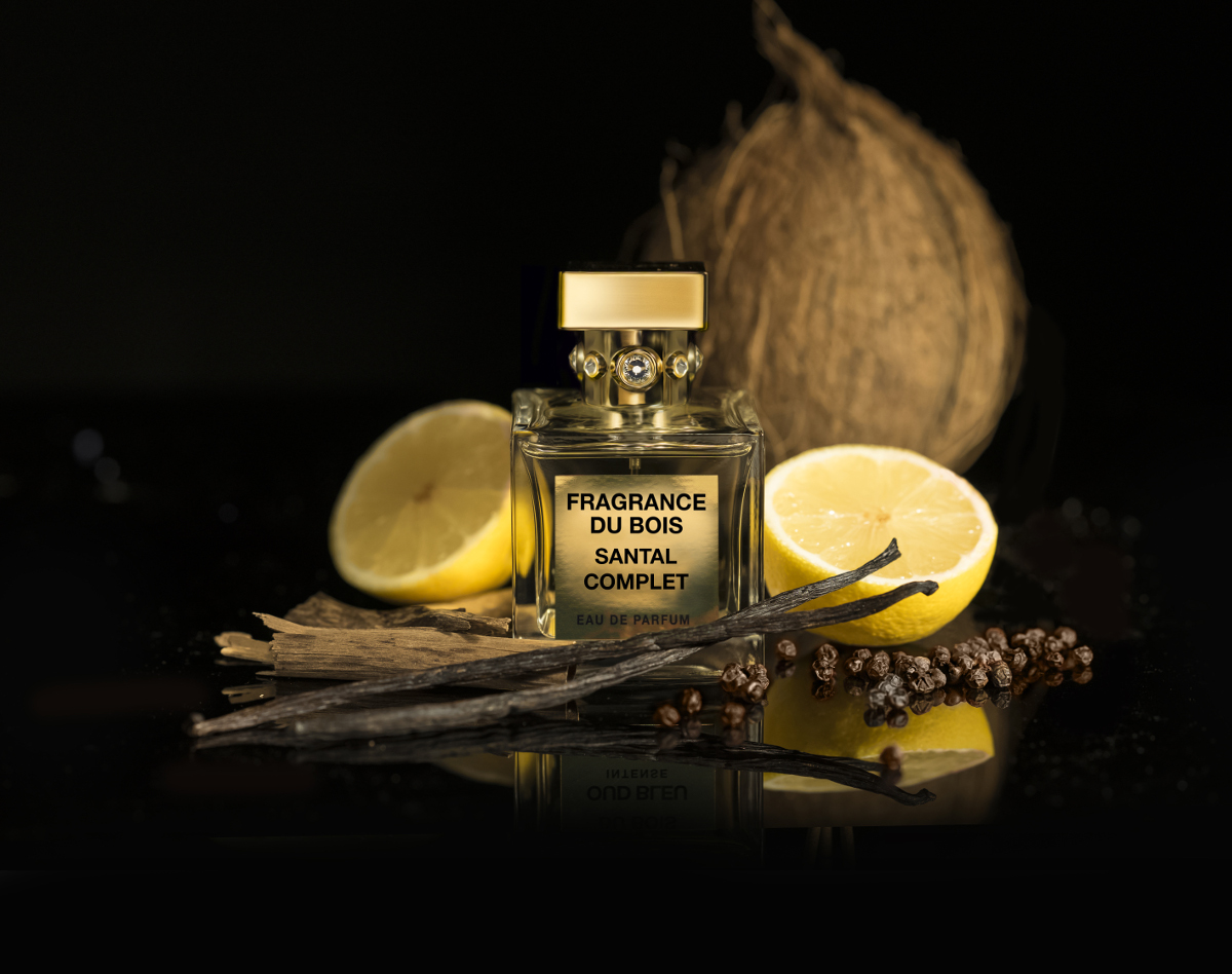 a bottle of Santal Complet next to vanilla pods, wood chips and a lemon