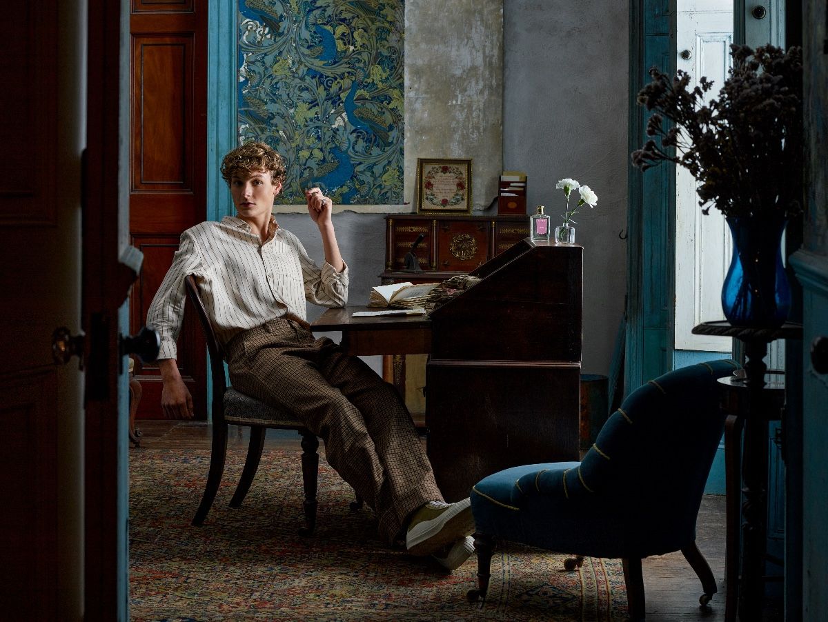 A handsome young man sat at an old fashioned desk surrounded by papers and perfume